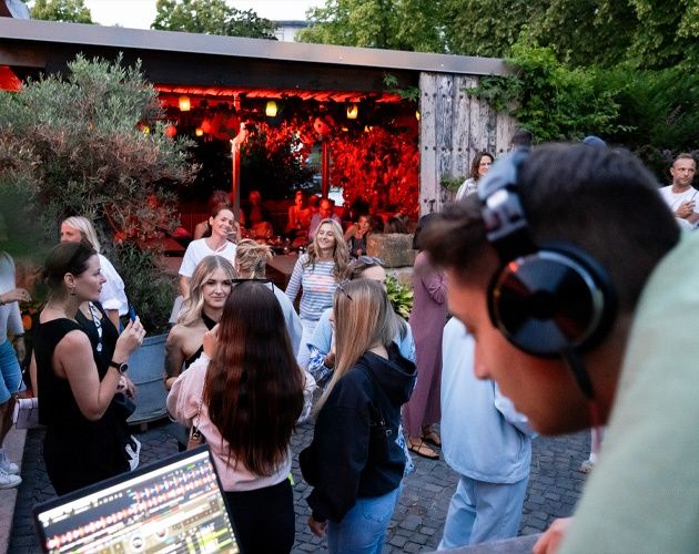 EIn DJ legt im Liebesbier Gastroigarten auf, Leute tanzen ausgelassen und genießen Cocktails.
