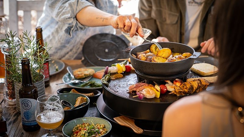 EIn gedeckter Tisch im Liebesbier Gastrogarten mit enem Tischgrill, auf dem die Gäste selbst Spieße, Kartoffeln und Fleisch zubereiten